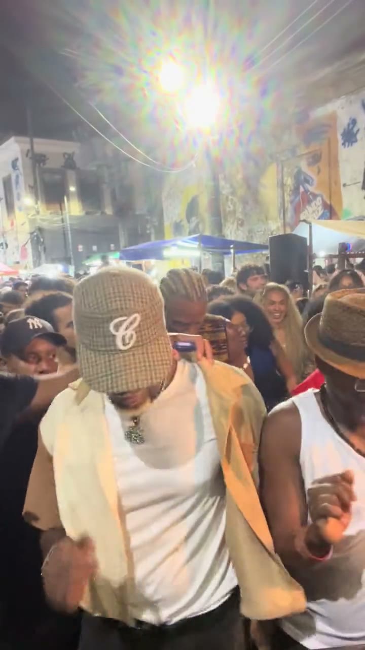 Original Baile Charme dance reference: the lead in a beige cap among a nighttime street crowd