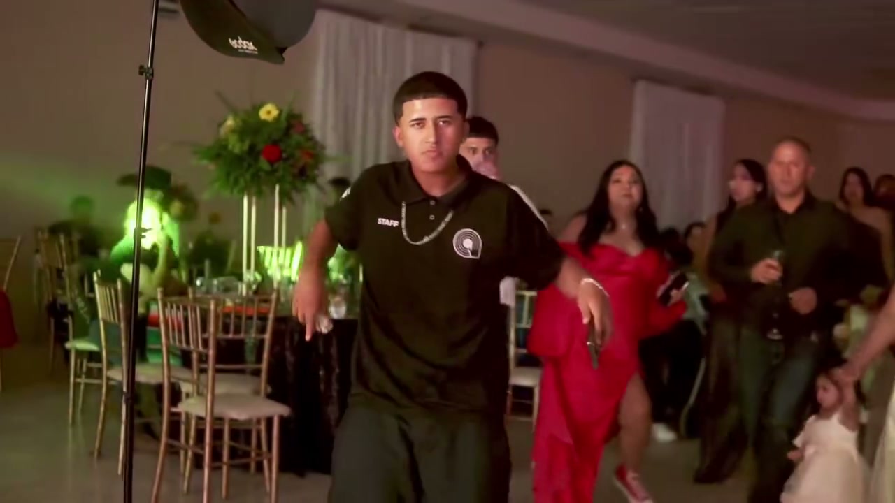 The original lead dancer in black walking toward the camera before turning back to the party