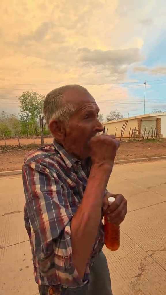 A roadside speaker holding an amber bottle, talking and gesturing under a warm cloudy sky