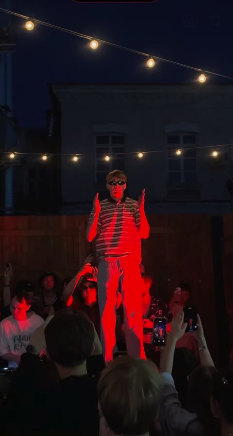 Central dancer holding both hands beside the face under red stage light
