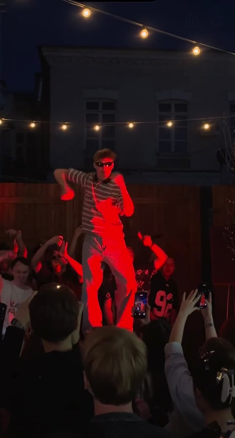 Central dancer under red light with spectators filming around the stage
