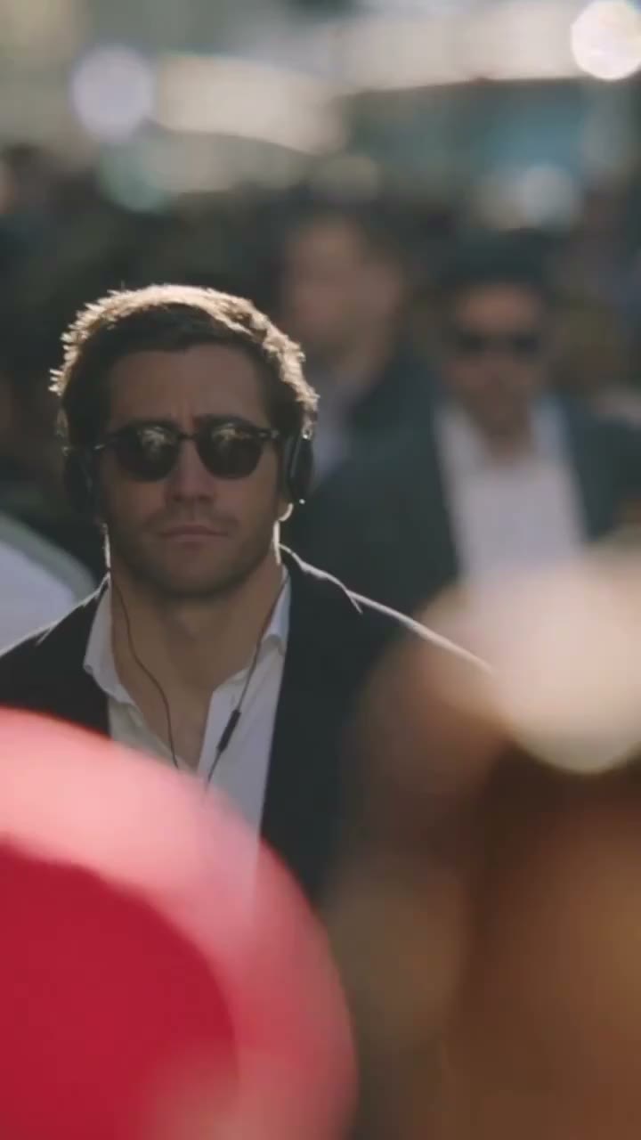 A central walker wearing sunglasses and headphones moving through a backlit street crowd