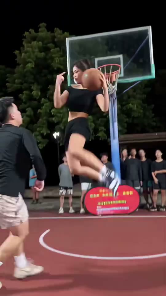 A ball-handler making an airborne taunting shot past a defender on a night court