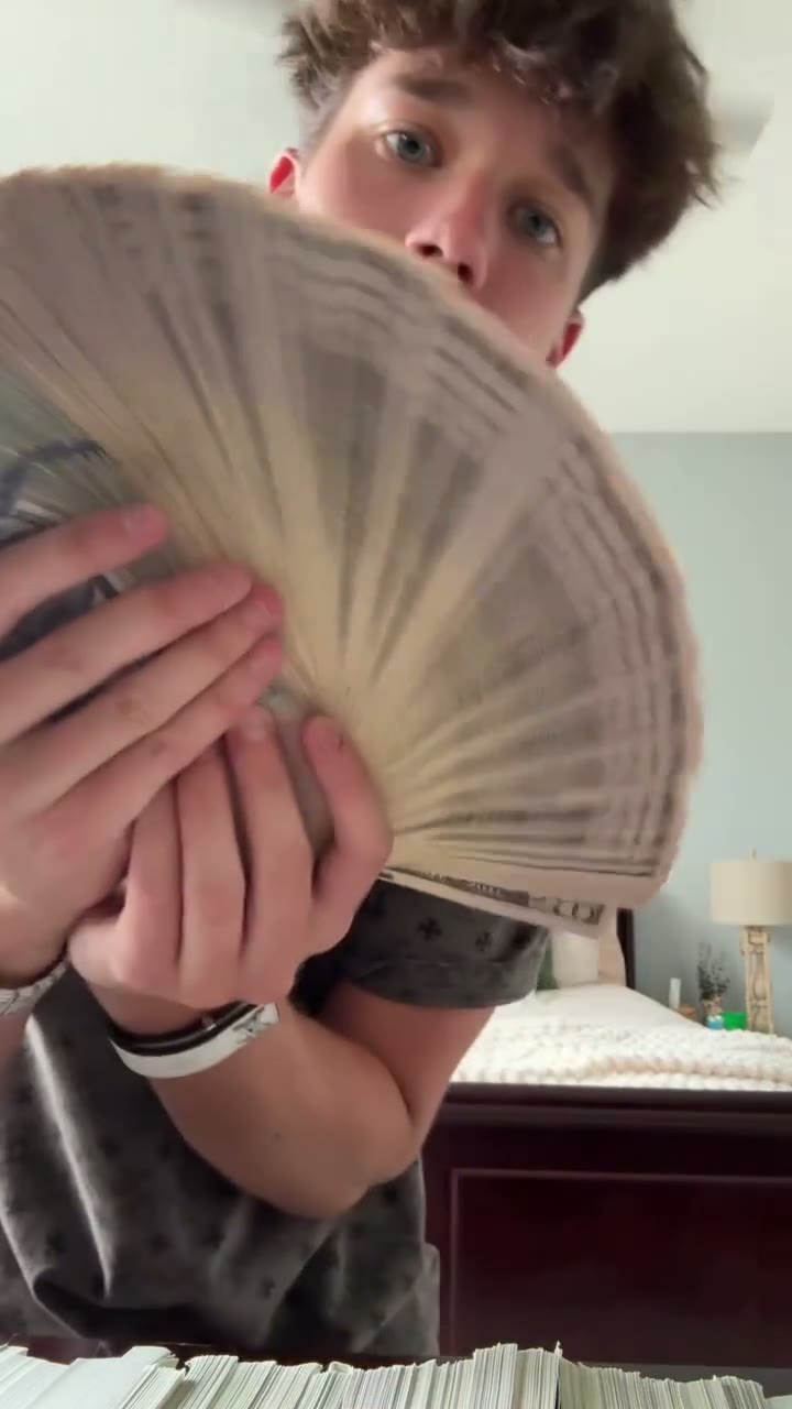 Money Spread reference performance with one person displaying stacks of cash and a fan of bills in a bedroom