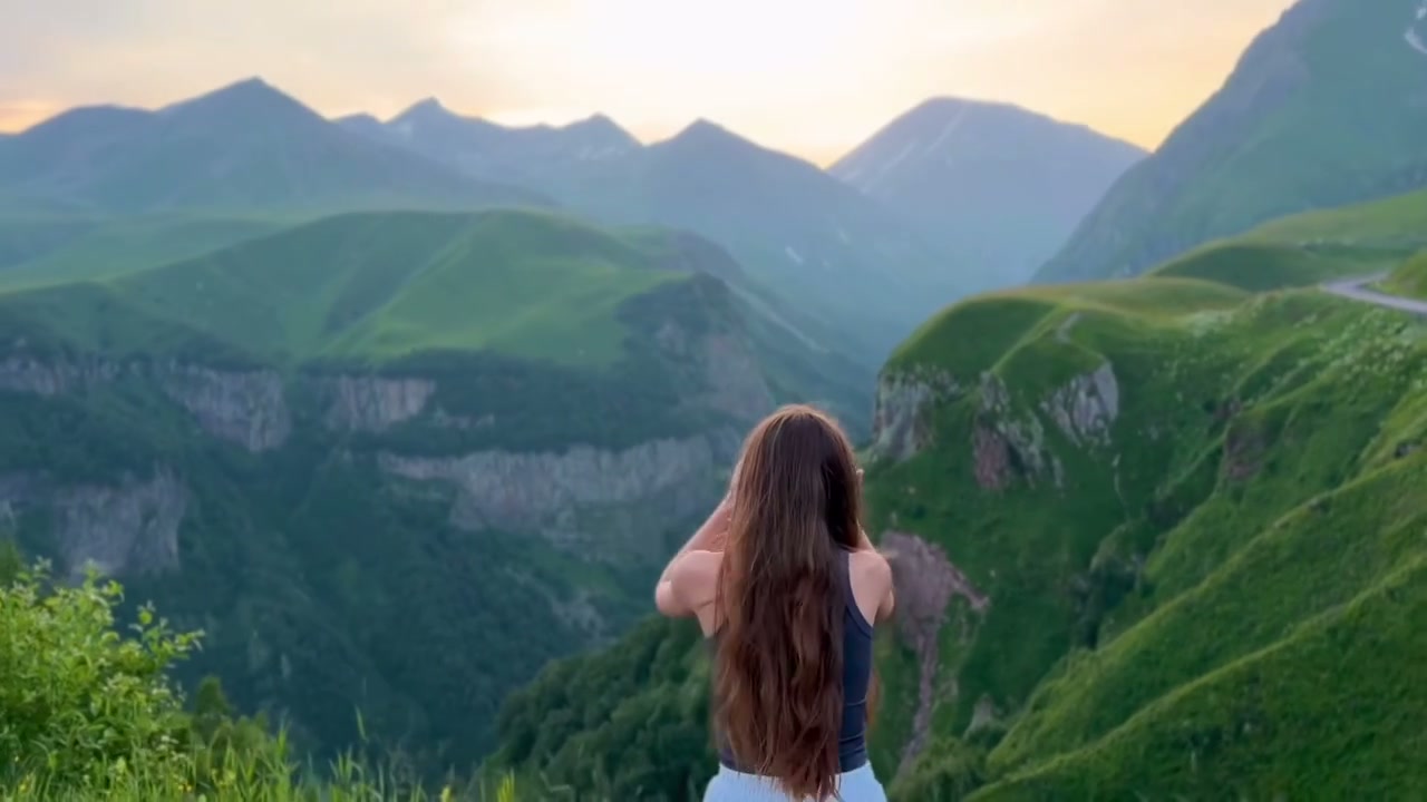 A two-person plaza gesture cuts to a mountain overlook where the central back-facing figure lifts their hands