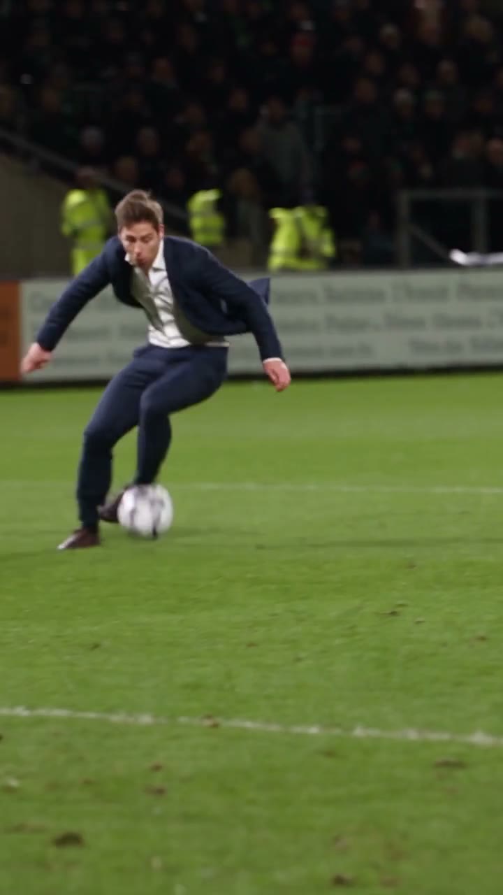 A character in a dark suit performing the Ozil goal sequence on a floodlit pitch