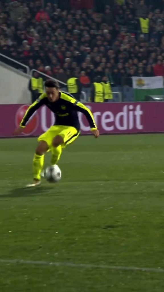 Ozil goal reference: a player in a dark shirt and yellow shorts chips the ball, beats the keeper, and shoots