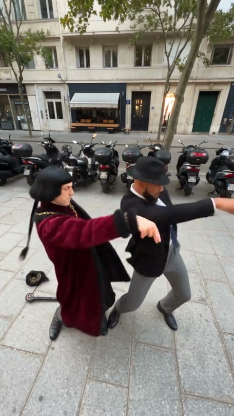 Dupla humana de Smalltown Boy AI trocando os papéis de dança do primeiro plano e do fundo numa rua ladeada de cafés