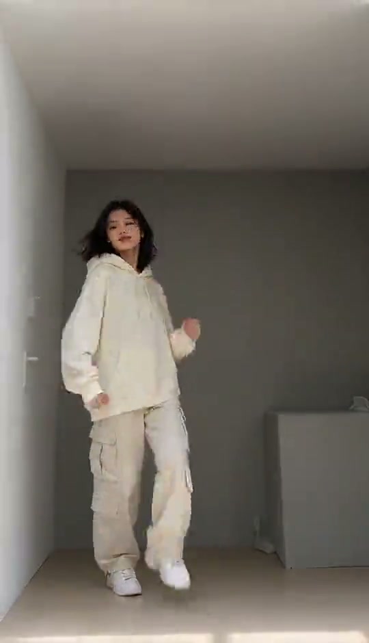 A solo dancer in a cream outfit performing bouncing steps in a plain room